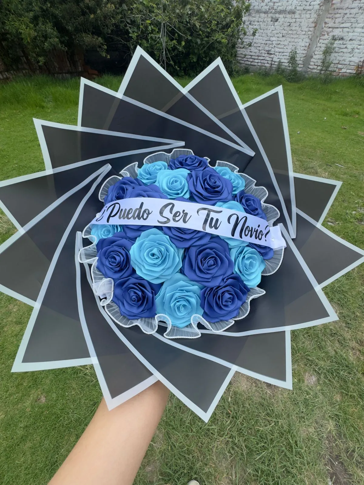 Ramo de rosas de cinta en dos tonos de azul, con envoltura negra en picos y una banda blanca con la frase «¿Puedo ser tu novio?».