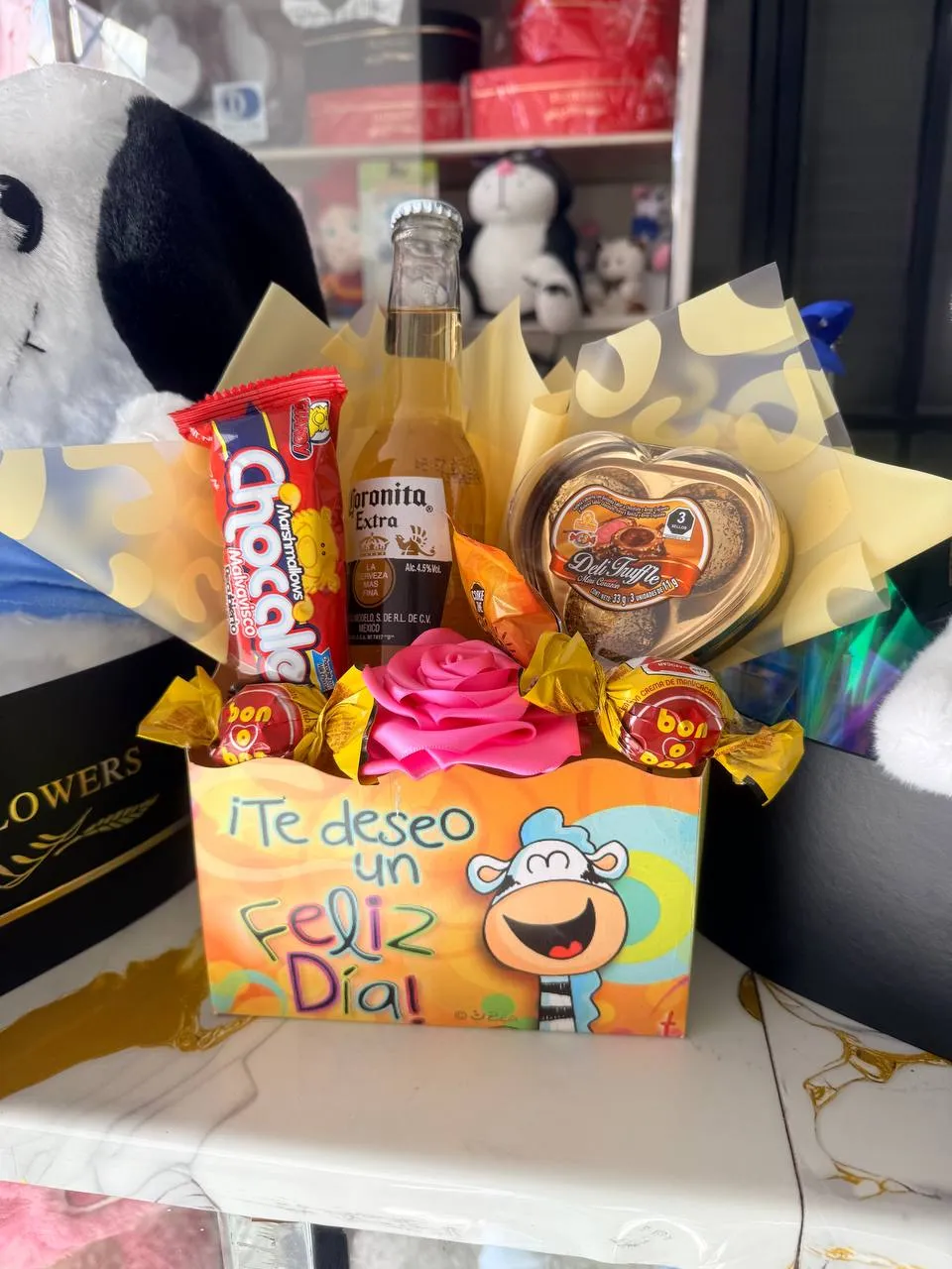 Caja de regalo con bebidas, chocolates y una tarjeta ilustrada.