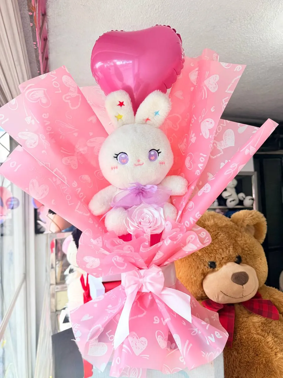 Arreglo con peluche de conejo, globo de corazón y envoltura rosa.