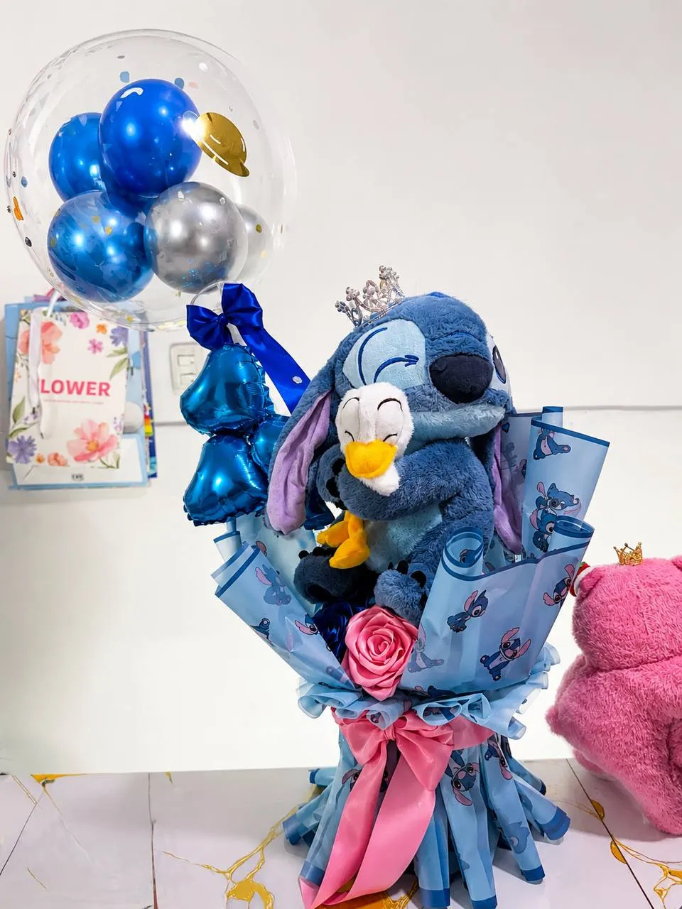 Ramo con un peluche azul, un globo burbuja con globos azules dentro y una rosa de cinta.