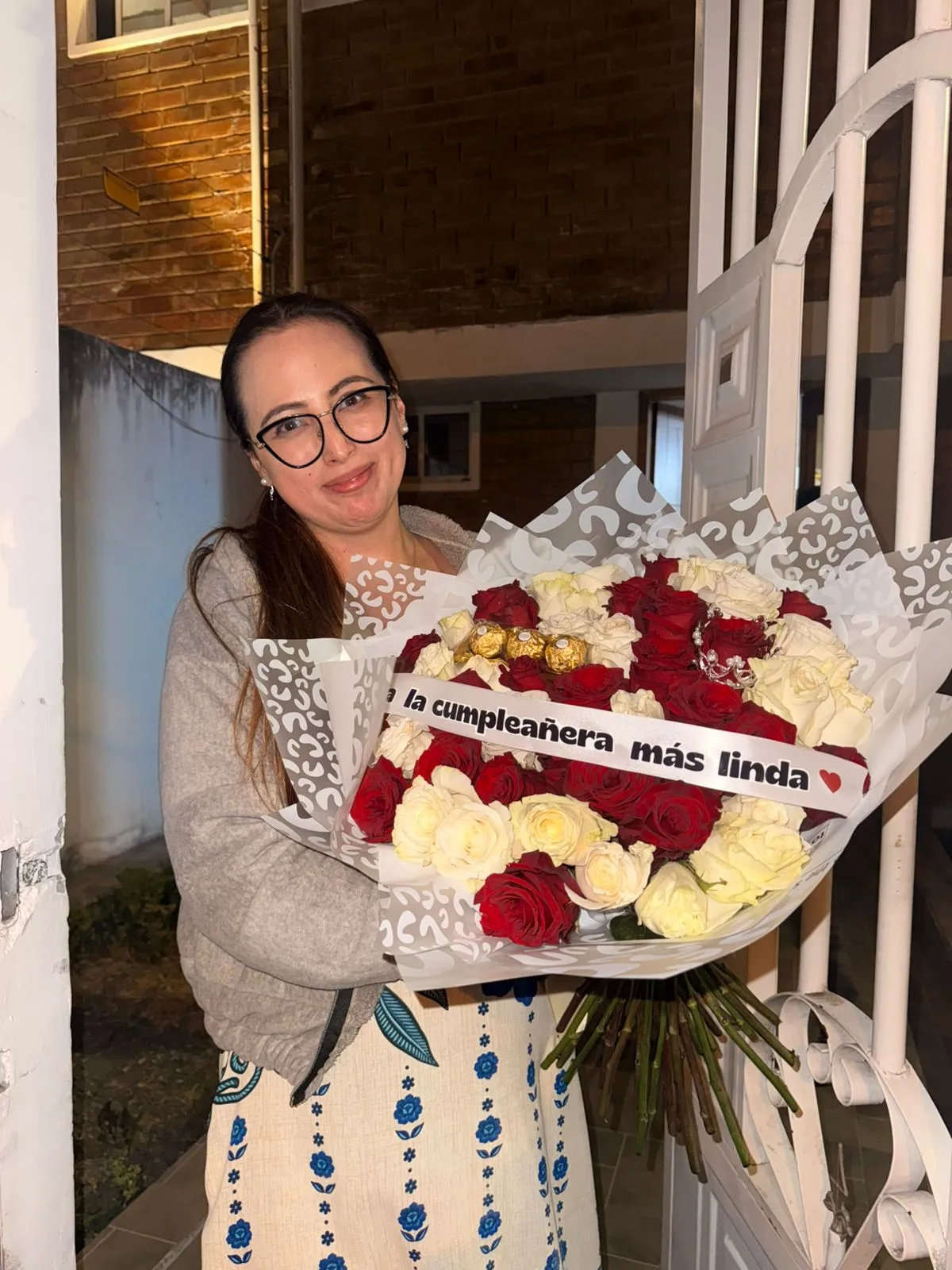 Una mujer sostiene un ramo de rosas rojas y blancas con chocolates y una cinta de cumpleaños.